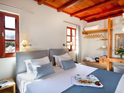 Camera luminosa con soffitto in legno, letto bianco e finestra con vista sul verde.