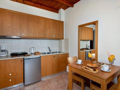 Piccola cucina con armadietti in legno, lavastoviglie, macchina per il caffè e tavolo da pranzo per due persone.