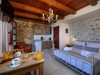 Camera accogliente con letto matrimoniale, soffitto con travi in legno, pareti in pietra e angolo cottura.