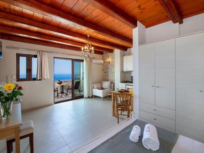 Camera d'hotel luminosa con soffitti alti con travi in legno, letto, tavolo, sedie e vista mare attraverso porte aperte.