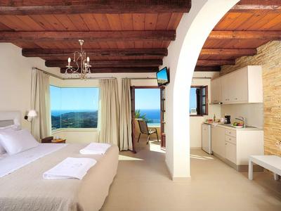 Camera d'hotel luminosa con soffitto a travi di legno, letto matrimoniale, angolo cottura e vista mare.