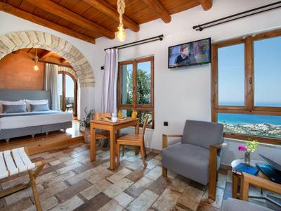 Camera d'albergo luminosa con travi in legno, poltrone, letto e grande finestra con vista mare.