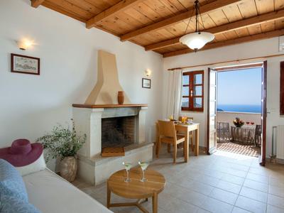 Soggiorno luminoso con camino, soffitto a travi in legno e vista mare tramite porte doppie aperte.