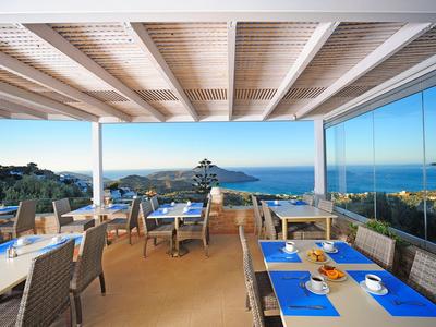Terrasse ouverte avec tables dressées offrant une vue sur la mer par ciel clair.