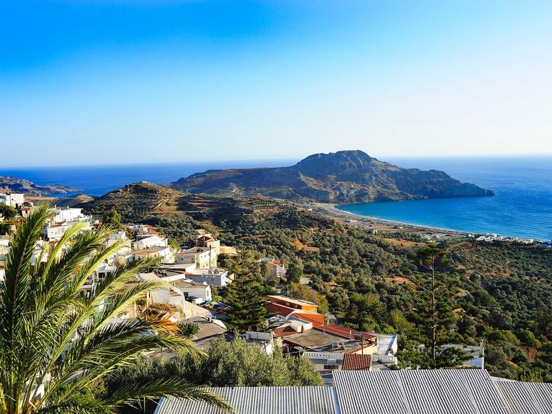 Vista su un paesaggio costiero con case, palme e mare sullo sfondo sotto un cielo limpido.