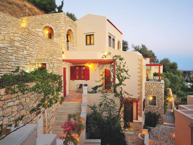 Casa mediterranea illuminata con muri in pietra e piante la sera.