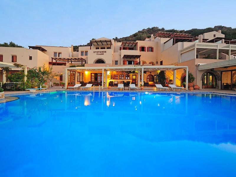 Hotel illuminato con grande piscina al crepuscolo in un paesaggio collinare.