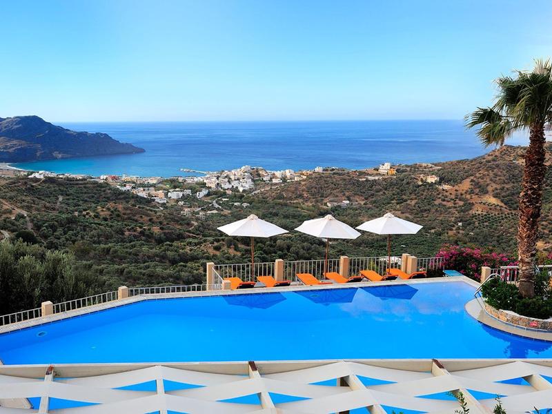 Piscina a sfioro con vista sul mare, palme e colline sotto un cielo limpido.