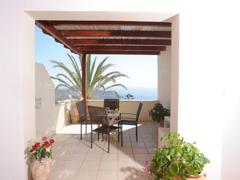 Terrazza coperta con sedie e tavolo con vista sul mare e palme.