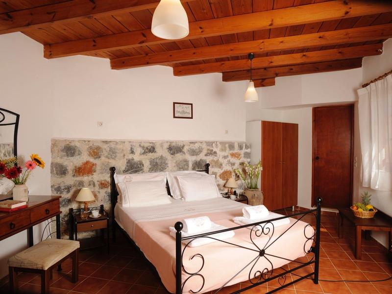 Camera accogliente con soffitto a travi di legno, letto in ferro battuto e parete in pietra.