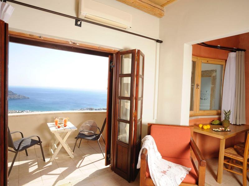 Camera luminosa con balcone aperto, vista mare, tavolo con sedie e zona soggiorno accogliente.