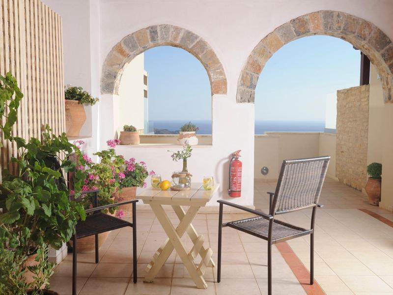 Terrazza soleggiata con due sedie, un tavolo e vista sul mare attraverso archi in pietra.