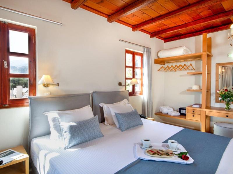 Camera luminosa con soffitto in legno, letto bianco e finestra con vista sul verde.