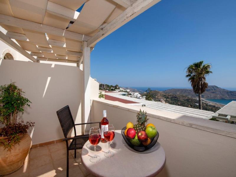 Balcone con tavolo, sedie e ciotola di frutta con vista sul mare e una palma.