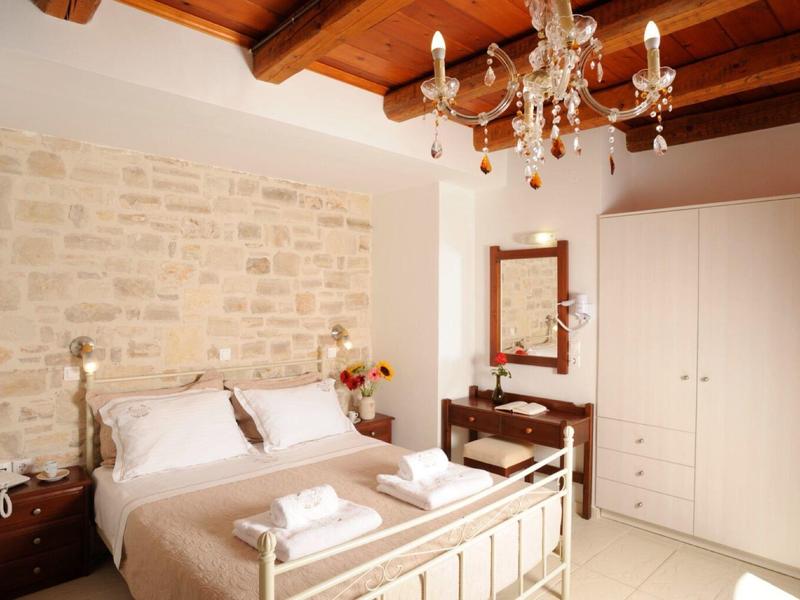 Camera d'hotel accogliente con letto matrimoniale, parete in pietra e soffitto con travi in legno.