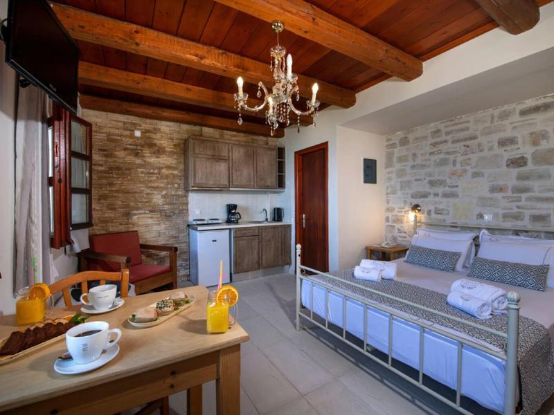 Camera accogliente con letto matrimoniale, soffitto con travi in legno, pareti in pietra e angolo cottura.