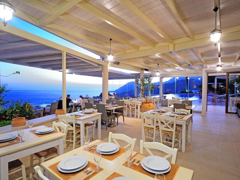Ristorante all'aperto con tavoli bianchi e vista sul mare al crepuscolo.
