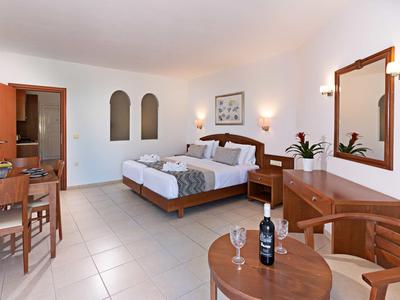 Helles Hotelzimmer mit Doppelbett, Holzmöbeln, Tisch mit Stühlen und Flasche Wein auf kleinem Tisch.