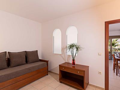 Kleiner Raum mit Sofa, braunem Möbelstück, Pflanze und Blick ins Esszimmer durch Türöffnung.