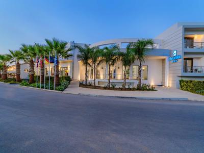 Nowoczesny budynek hotelowy z palmami i oświetlonym wejściem o zmierzchu.