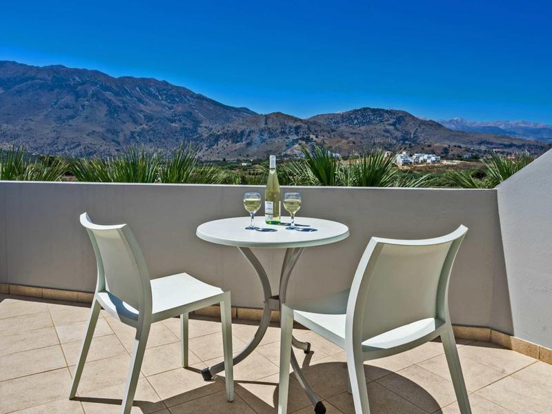 Terrasse mit kleinem runden Tisch, zwei weißen Stühlen und Blick auf Berge unter klarem Himmel.