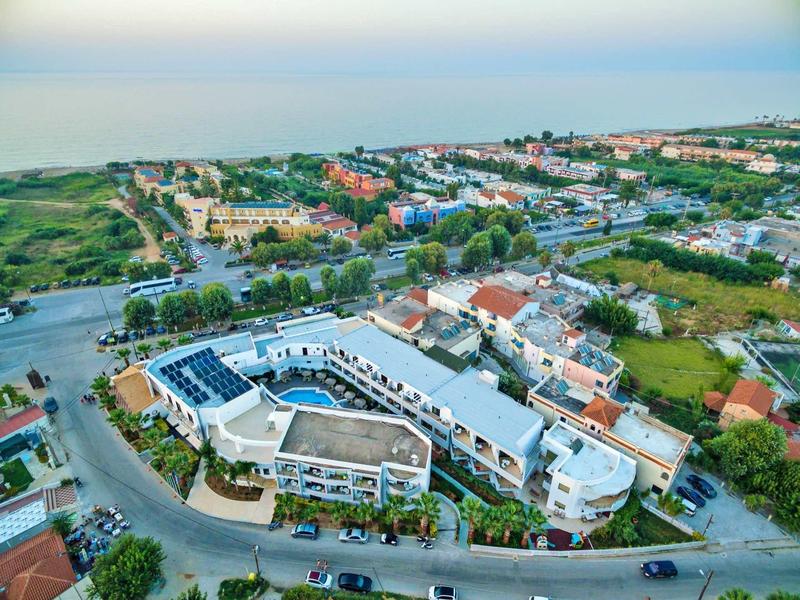 Luftaufnahme eines Wohnkomplexes mit weißen Gebäuden, roten Dächern und Solarpaneelen, umgeben von Grün.