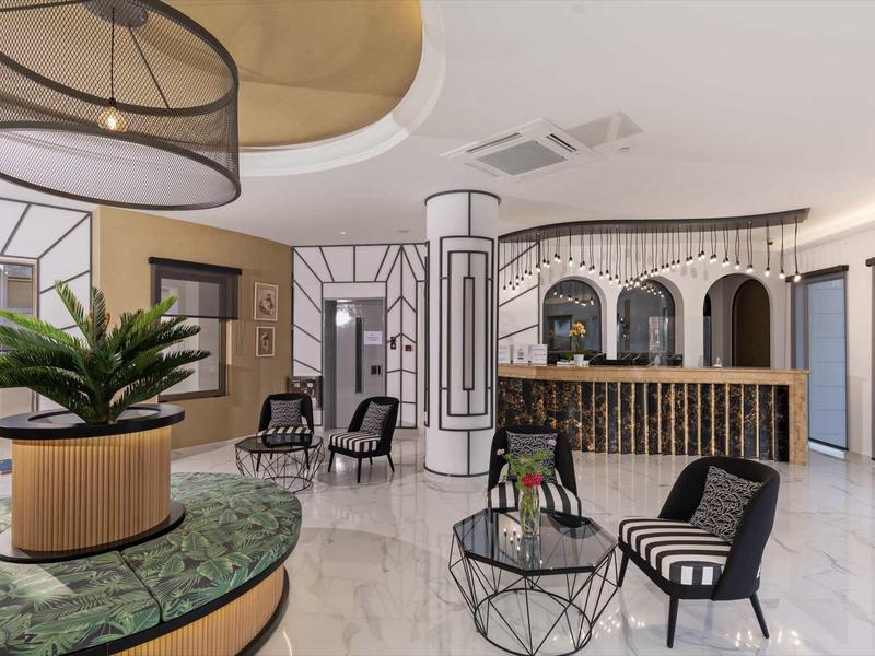 Moderner Hotel-Lobby mit Marmorboden, Schwarz-Weiß-Möbeln, Pflanzen und runden Deckenleuchten.