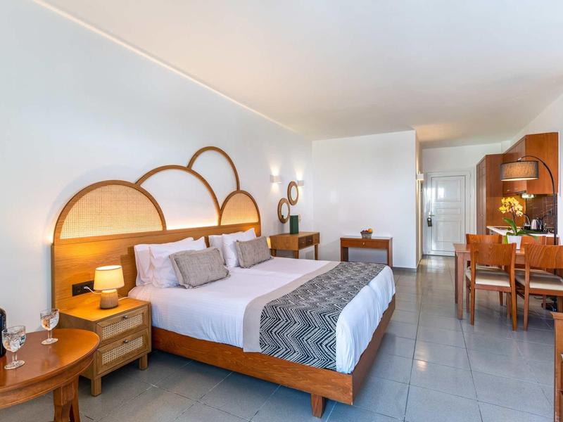 Schlafzimmer mit Doppelbett, Holz-Möbeln, gemütlicher Dekoration und Essbereich im hellen Raum.