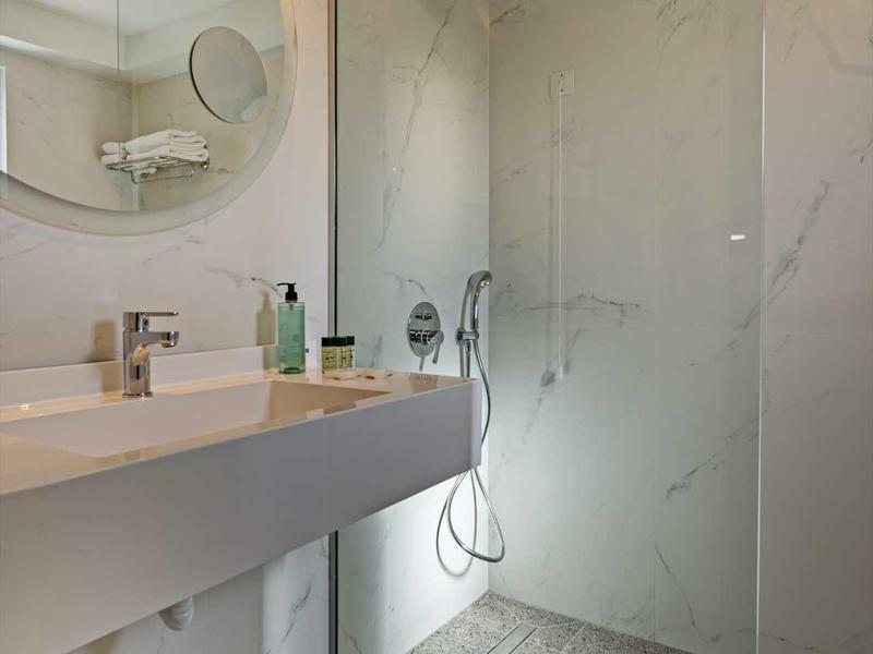 Moderne, helle Badezimmer mit Glasdusche, rundem Spiegel, weißem Waschbecken und minimalistischer Gestaltung.