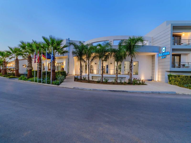 Modernes, zweistöckiges Hotel mit Palmengarten und breiter Zufahrt bei Dämmerung.