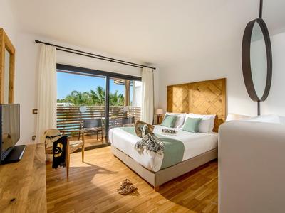 Chambre d'hôtel lumineuse avec lit double, meubles en bois et balcon avec vue sur les palmiers.