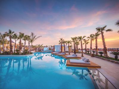 Piscina a sfioro con lettini e palme al tramonto in un resort di lusso.