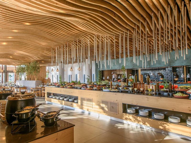 Buffet moderne avec plafond ondulé en bois et large choix de plats dans un restaurant lumineux.