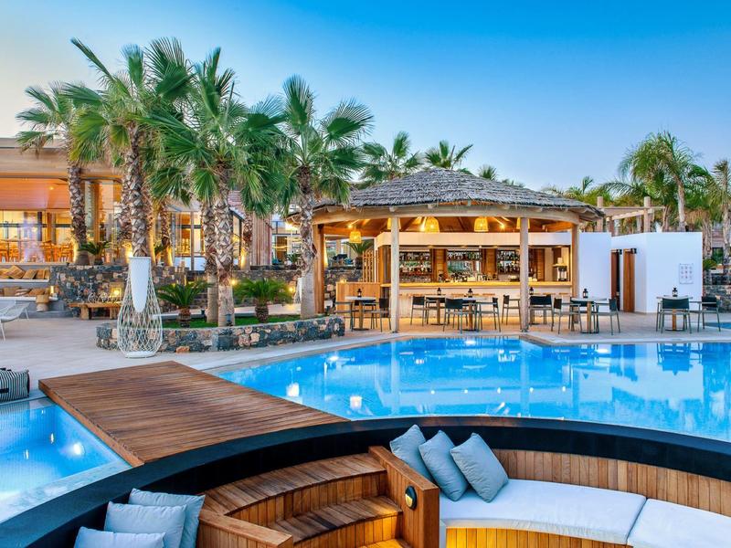 Hôtel luxueux avec grande piscine, palmiers et salon confortable sous un ciel bleu.