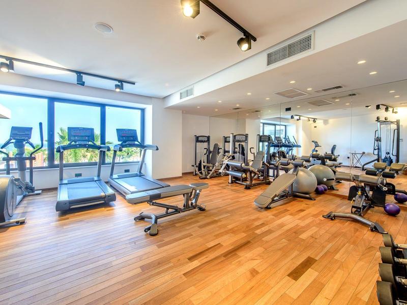 Salle de sport moderne avec tapis de course, haltères et équipements d'entraînement sur parquet.