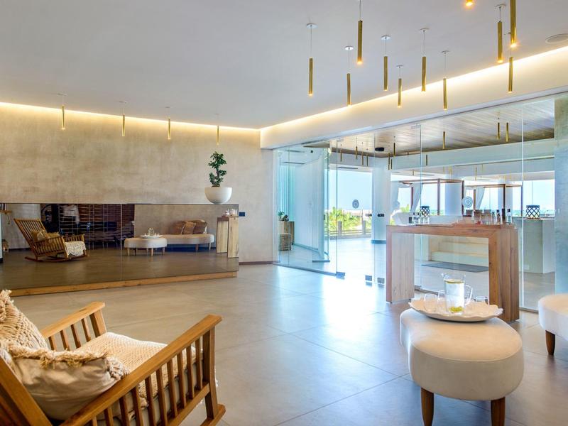 Espace lounge d'hôtel moderne et lumineuse avec chaises, tabourets et grand miroir mural.