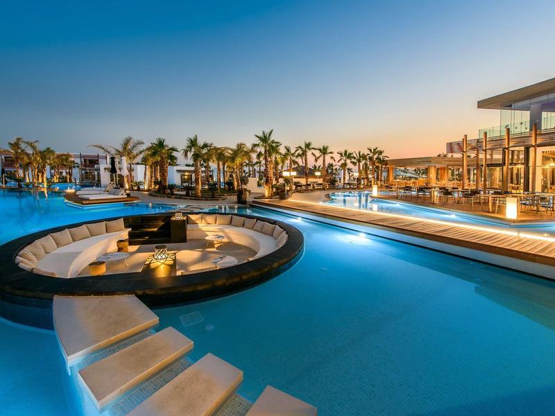 Piscine extérieure avec jacuzzi éclairé et espaces détente au coucher du soleil dans un complexe hôtelier.