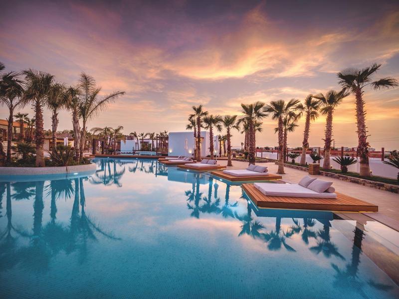 Chambre d'hôtel lumineuse avec lit double, meubles en bois et balcon avec vue sur les palmiers.