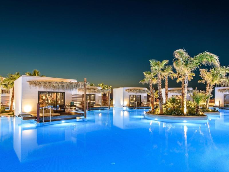 Piscine d'hôtel éclairée avec palmiers et villas modernes de nuit