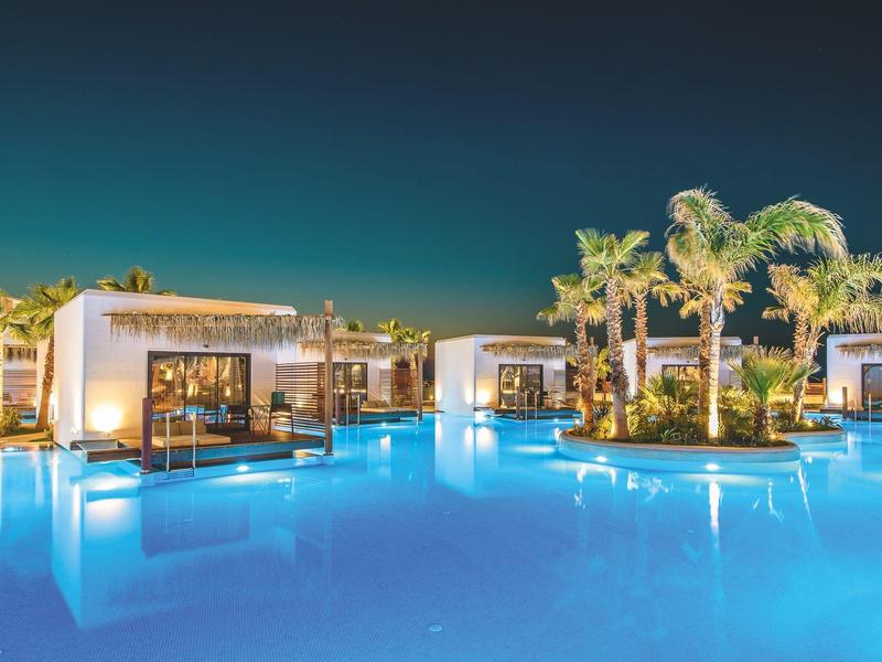 Complexe hôtelière de luxe avec piscine éclairée et palmiers la nuit.