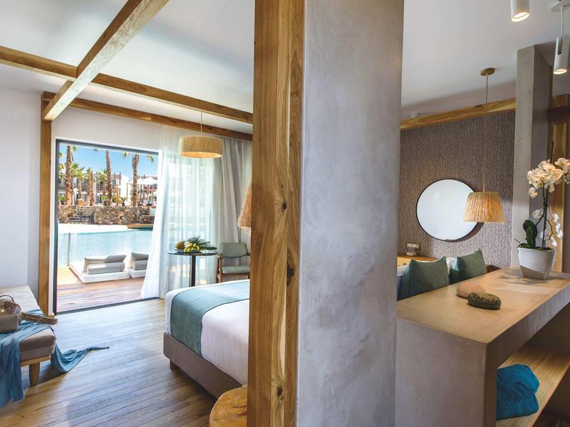 Chambre d'hôtel moderne avec lit double, décoration en bois et vue sur une terrasse avec piscine.