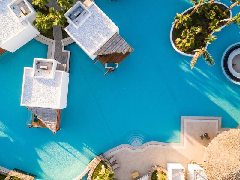 Vue d'ensemble d'une piscine avec trois bungalows sur l'eau et des transats au bord.