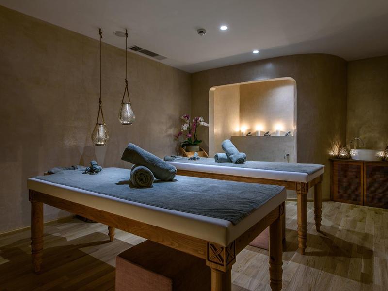 Salle de massage calme avec deux tables, lumière chaude et ambiance cosy.
