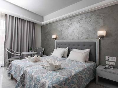 Camera d'albergo moderna con letto matrimoniale, comodino e balcone illuminato dalla luce naturale.