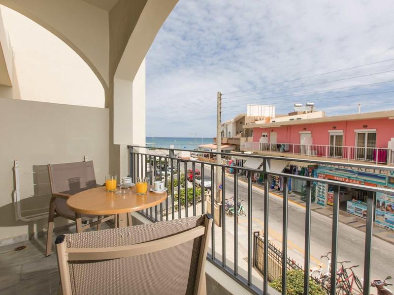 Balcone con posti a sedere che si affaccia su una strada con edifici e il mare sullo sfondo.