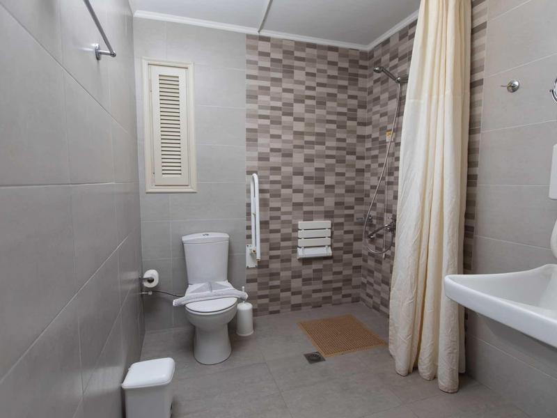 Bagno accessibile con WC, doccia, tenda e lavabo in tonalità neutre.