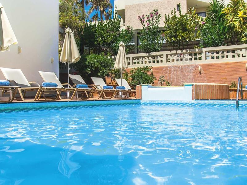 Piscina azzurra limpida con lettini e ombrelloni accanto a un hotel.