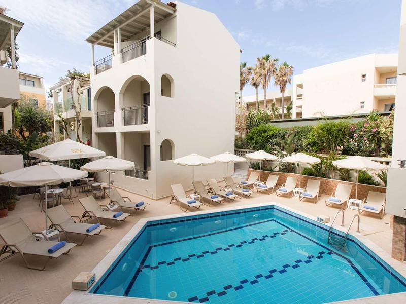 Hotel con piscina esterna, lettini e ombrelloni accanto a edifici bianchi con archi.