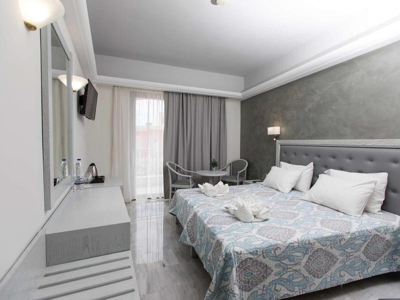 Camera d'hotel moderna con letto matrimoniale, zona soggiorno e balcone con tende.