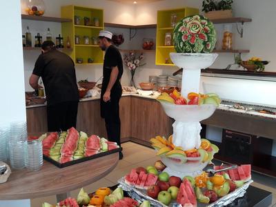 Buffet met vers fruit en watermeloenstukken in een lichte kamer met twee mensen achter de balie